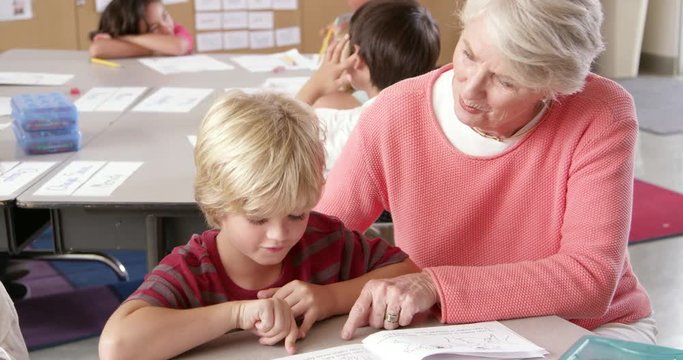 Senior teacher helps young schoolboy in class, elevated view