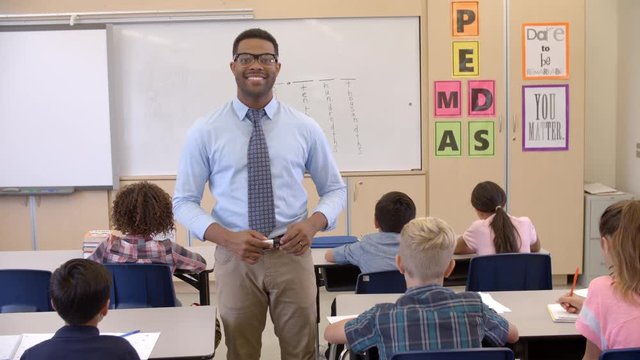 Happy black male teacher walking through class toward camera