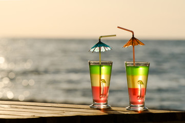 Two colored cocktail on a wooden table on the beach in the morning sun, the empty space