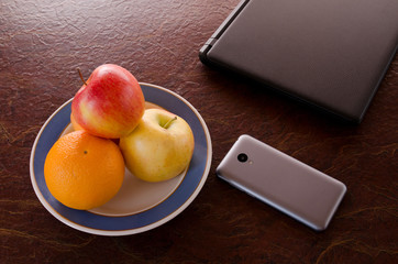 Dish of fruit, a smartphone, a laptop on the table, top view