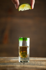 Squeezing lime into shot of tequila. Selective focus. Blurred background.