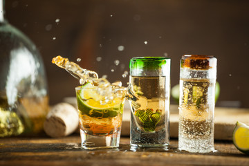 Shot glass of tequila splashing on wood table with lime. Selective focus, blurred background.