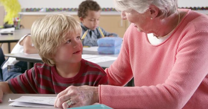 Senior female teacher helping young schoolboy in class