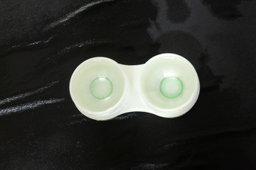 This is a photograph of Green contact lenses placed in a case above a surface soaked in contact lenses solution