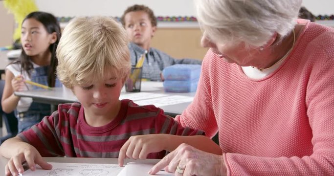 Senior female teacher helps young schoolboy reading in class