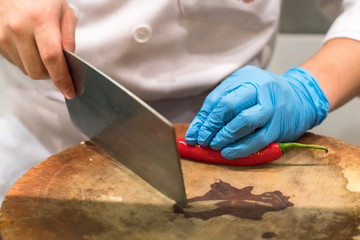 Hand slicing Chili pepper with Knife on chopping board
