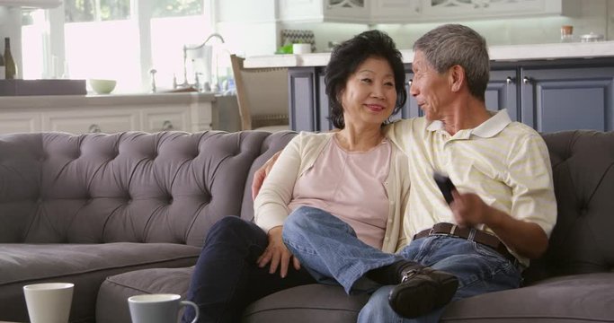 Senior Asian Couple At Home On Sofa Watching TV 
