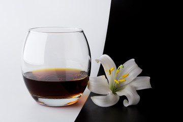 A glass of whiskey and a lily flower on black and white background