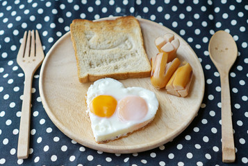 Breakfast consist of fried egg in shape of heart and happy bread