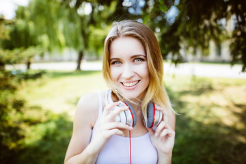 Teenage girl with headphones  outdoors on sunny summer day smiling. Beautiful millennial young woman listening to music relaxing. Horizontal, retouched,