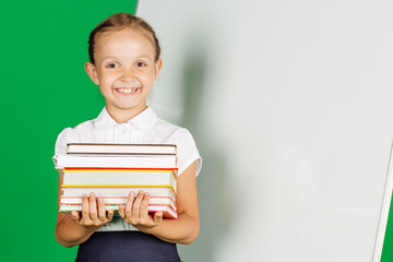 Girl in a school uniform near whiteboard with books . Learning, idea and school concept. Image on green background.

