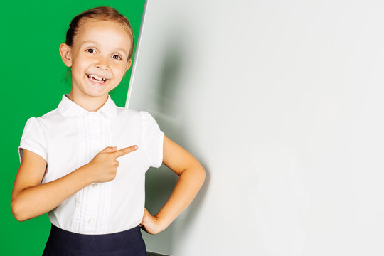 portrait of school girl in a school uniform near whiteboard with pointing at the whiteboard. Learning, idea and school concept. Image on green background.