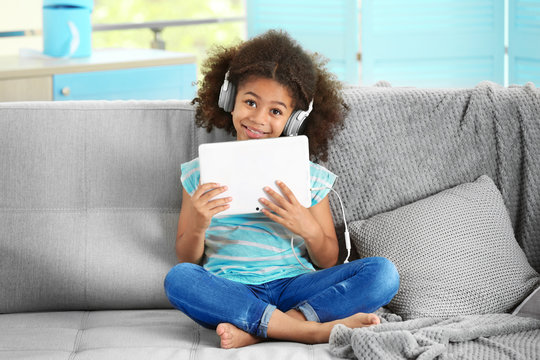 Cute African girl with tablet on couch