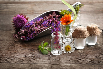 Composition with healing flowers and small glass bottles on wooden background