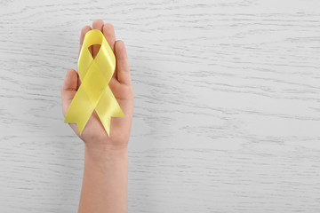 Woman hand with yellow ribbon on wooden background. Children cancer concept