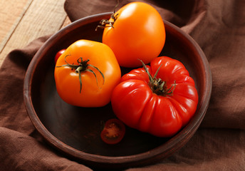 Juicy tomatoes in wooden plate on brown tablecloth