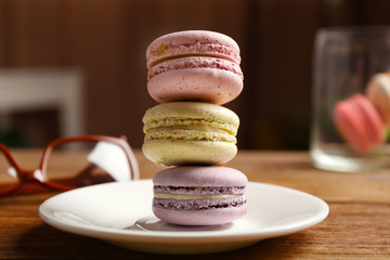 Tower of tasty macaroons in white plate on wooden table