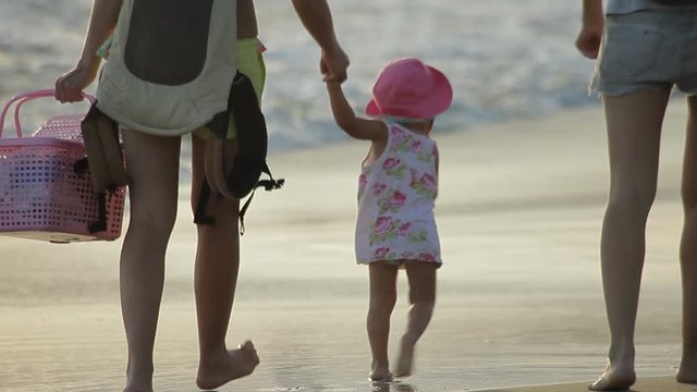 Mother with pretty baby girl and their friend are walking along the seacoast.