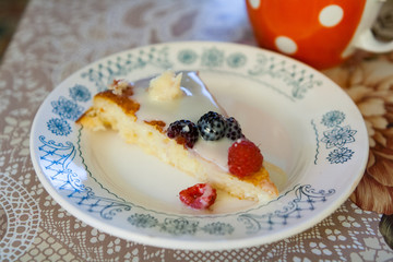 Piece of sweet cake with berries and cream sauce on a plate on a rustic kitchen.