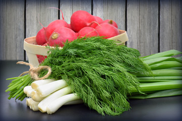 red radishes, green onions and dill on wooden table.