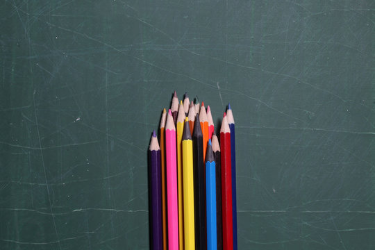 colorful pencils on green blackboard or desk