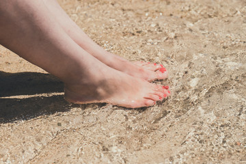 female feet with red pedicure in beach sand, close up