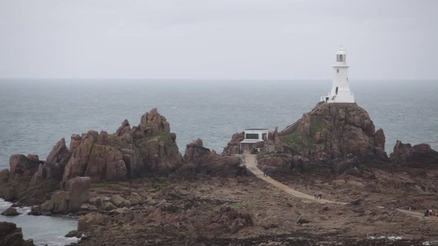 View of a lighthouse on Jersey island, with unrecognizable people walking by. 