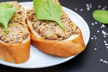 Sandwiches with pate and spinach leafs in white plate on black t
