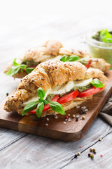 Wholegrain croissants with mozzarella, tomato and pesto on wooden table, selective focus