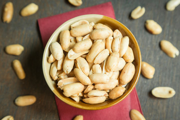 Roasted peeled salted peanuts in rustic bowl on wooden background (focus on peanut in bowl)