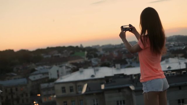 Charming tourist taking photograph of the urban city at sunset, view from roof