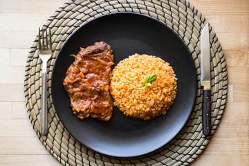 Steak with tomato sauce and bulgur rice in a black plate