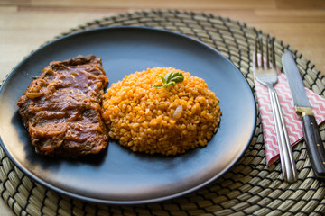 Steak with tomato sauce and bulgur rice in a black plate