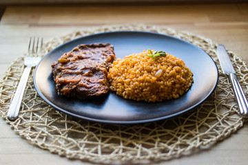 Steak with tomato sauce and bulgur rice in a black plate