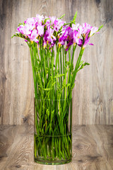 Freesia flowers in the vase on wooden background