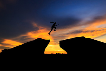 Man jump through the gap between hill.man jumping over cliff on sunset background,Business concept...