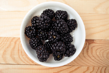 Blackberries in a white plate on a wooden board