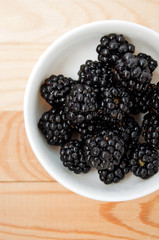 Blackberries in a white plate on a wooden board