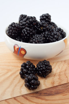Blackberries in a white plate on a wooden board