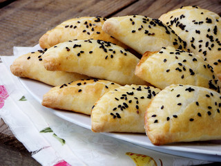 homemade pies sprinkled with black sesame seeds on a plate on a wooden background