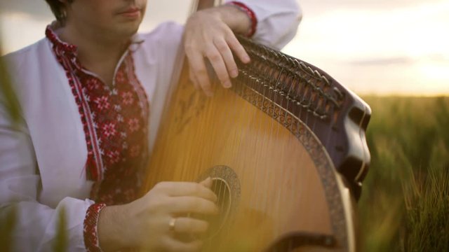 Young man playing pandora in wheat field at sunset. Close up.