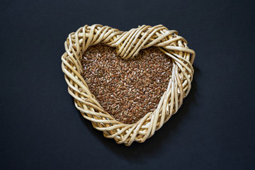 Flax seed in woven heart-shaped basket on dark background. Copy space