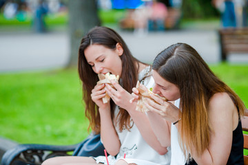 Caucasian women eats hamburger fast food sandwich on the street outdoors. Active girls hungry and eating street food after long walk