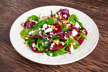 Healthy Beet Salad with fresh sweet baby spinach, kale lettuce, nuts, feta cheese on wooden table.