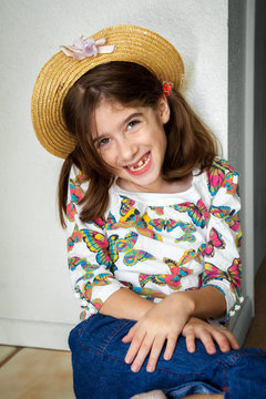 A cute young snaggletooth girl smiles with her while leaning up against a wall with hands crossed at her wrists.