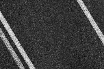 Level asphalted road with a dividing white stripes. The texture of the tarmac, top view.