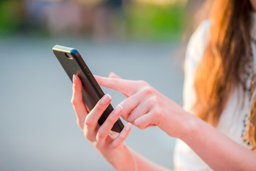 Closeup of female hands is holding cellphone outdoors on the street in evening lights. Woman using mobile smartphone.