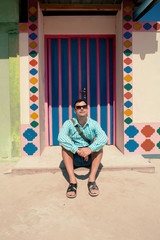 Young brunette man, wearing in blue shirt, sandals, sunglasses, with bag