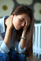 Young tired woman sitting on the bed near children's cot.