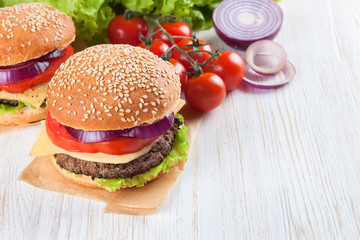 Homemade cheeseburger on white wooden surface.
